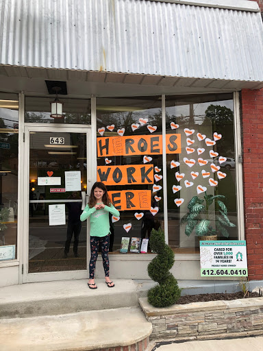 A child stands in front of a store with a colorful window display celebrating heroes and community workers.