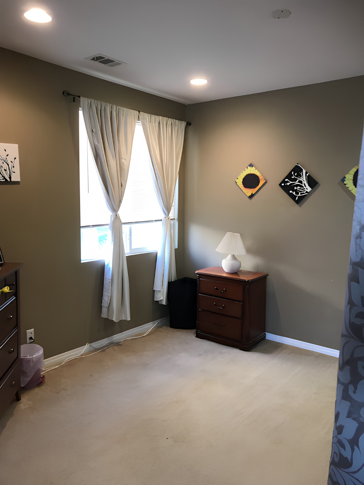 A cozy bedroom with a dresser, lamp, and decorative wall art.