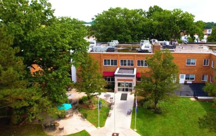 Aerial view of a brick building surrounded by trees with a pathway leading to the entrance.
