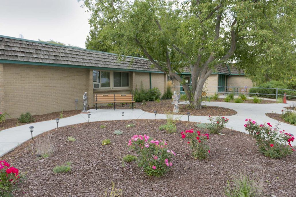 A quaint house with a beautifully landscaped front yard featuring trees, flowers, and a pathway.