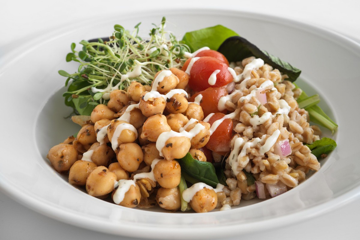 A healthy salad bowl with chickpeas, grains, cherry tomatoes, greens, and sprouts drizzled with dressing.