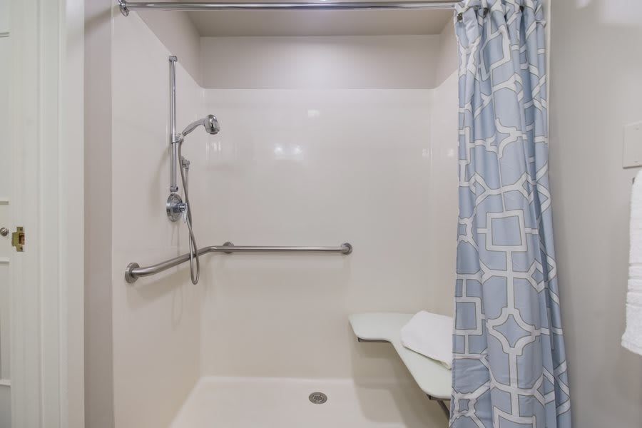 An accessible shower with a handrail, seat, and curtain.