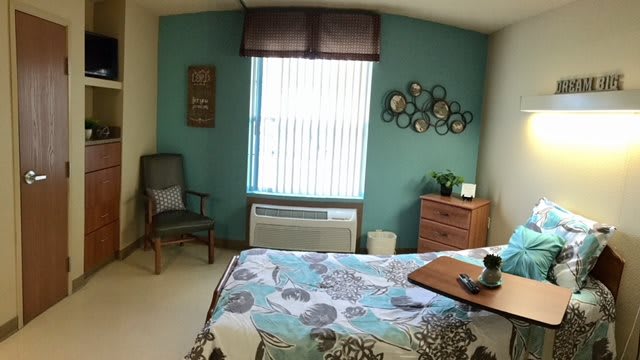 A cozy bedroom with teal accent wall and floral bedspread.