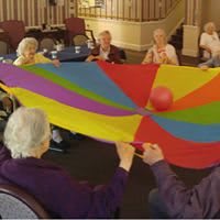 A group of elderly individuals engaging in a colorful parachute activity indoors.