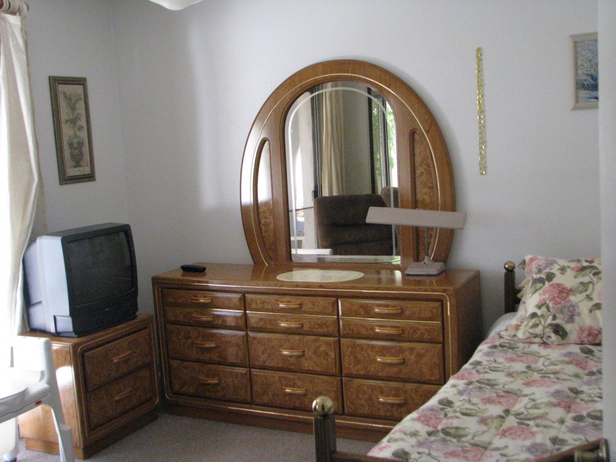 A bedroom with a wooden dresser and mirror, a television, and a floral bedspread.