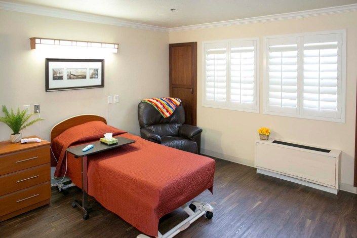 A cozy room with a hospital bed, leather chair, and a window dressed in shutters.