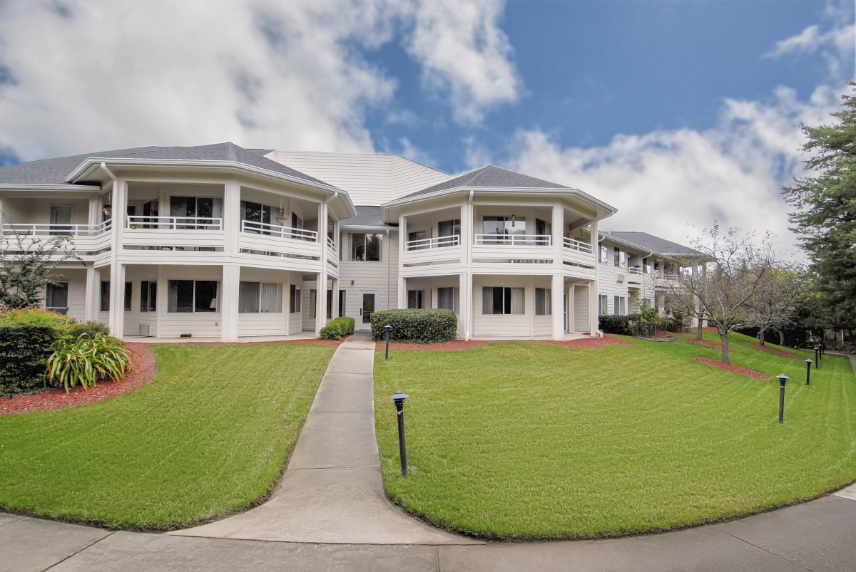 A large residential building with a well-maintained lawn and a cloudy sky backdrop.