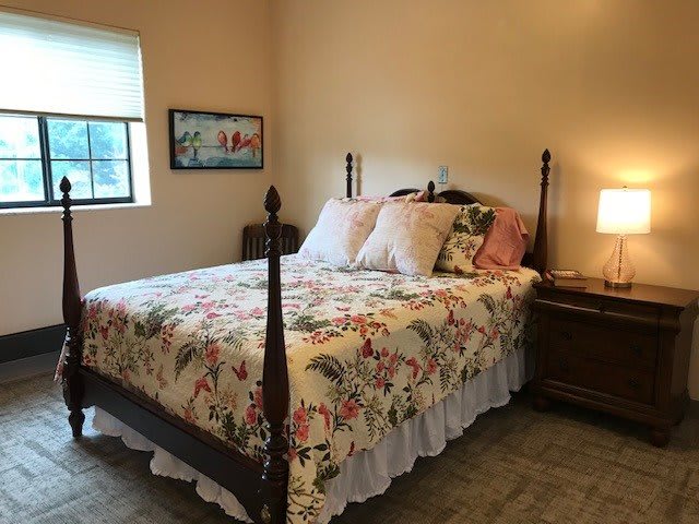 A cozy bedroom with a floral quilt on the bed and a lamp on the bedside table.