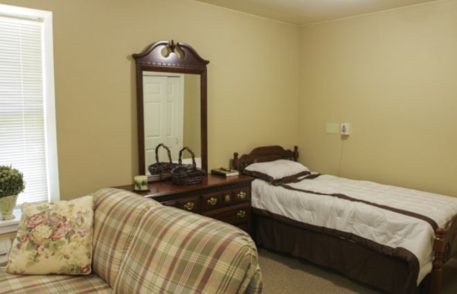 A cozy bedroom with a single bed, dresser with mirror, and a plaid couch.