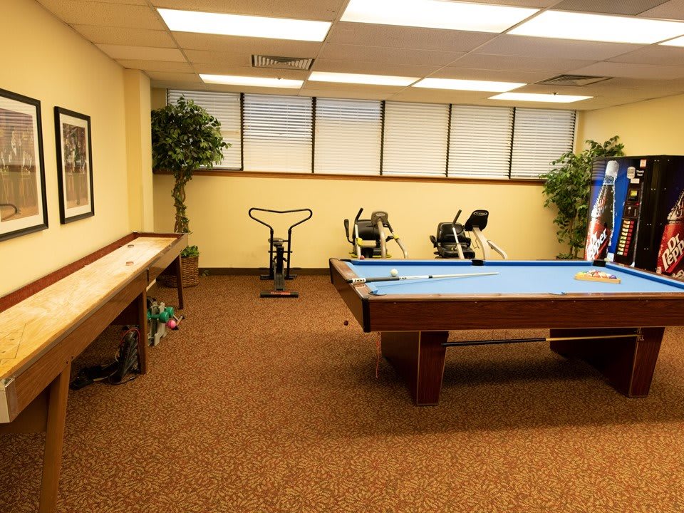 A recreational room featuring a pool table, shuffleboard, and exercise equipment.