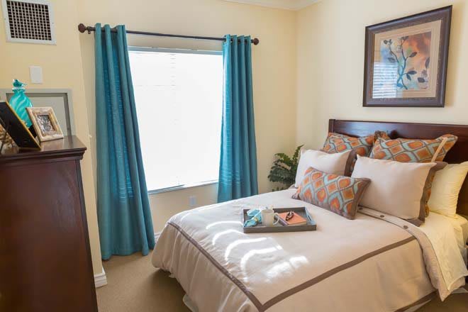 A cozy bedroom with a neatly made bed, adorned with decorative pillows, and teal curtains framing the window.