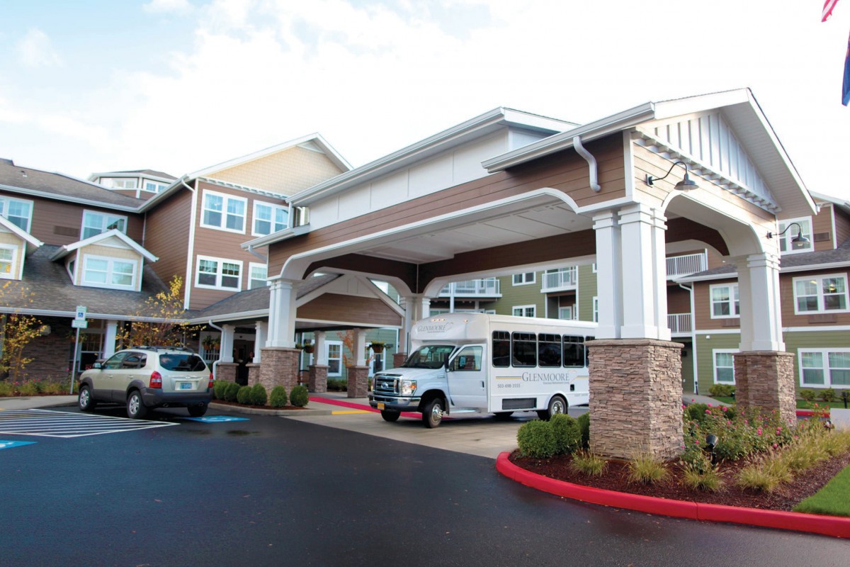 A residential building entrance with parked vehicles in the driveway.