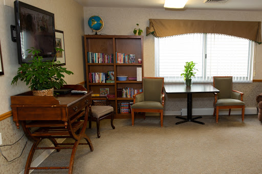 A cozy reading area featuring a bookshelf, comfortable chairs, and a small table, illuminated by natural light.