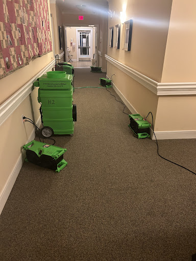 A hallway lined with green drying machines, likely used for drying out the carpet.