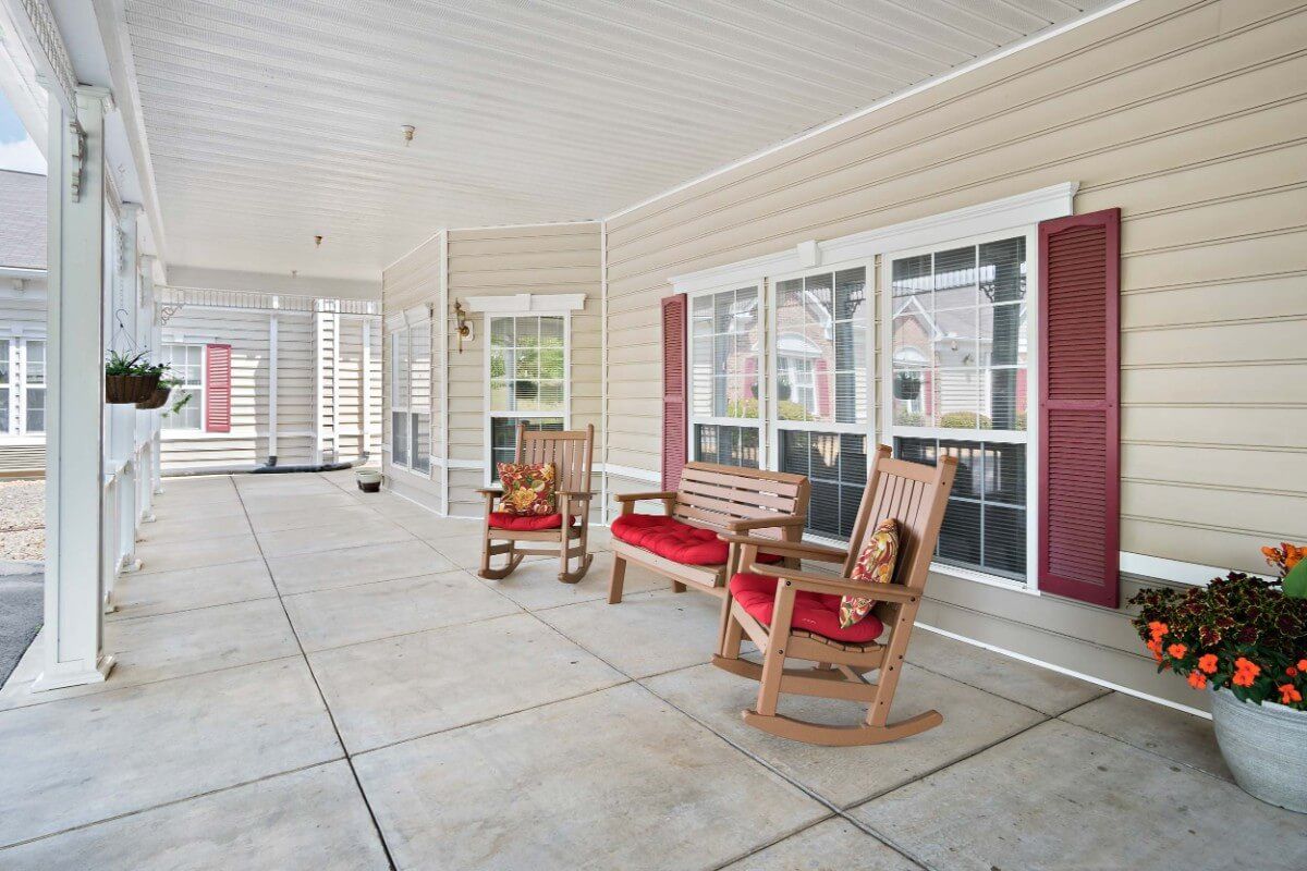 A cozy covered porch with wooden rocking chairs and a bench, ideal for relaxation.