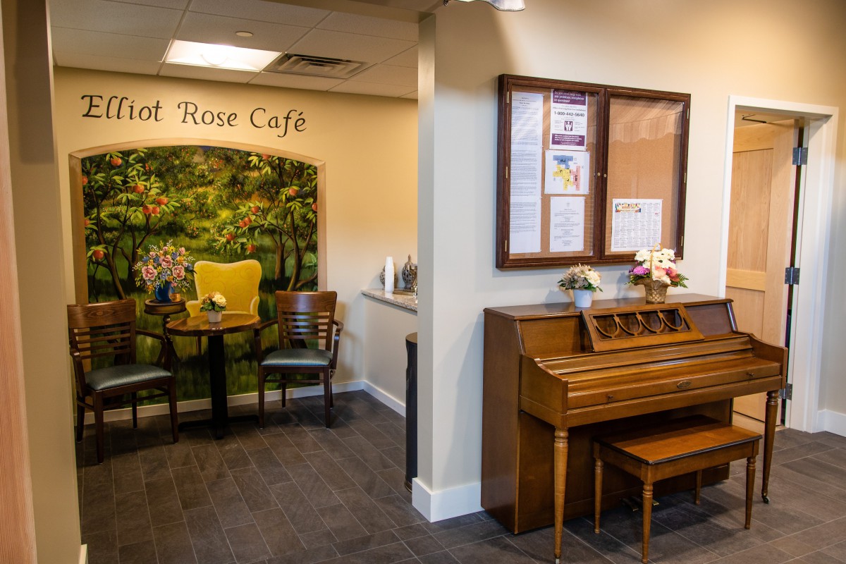 A cozy indoor cafe setting featuring a piano and a small seating area with chairs and a table.