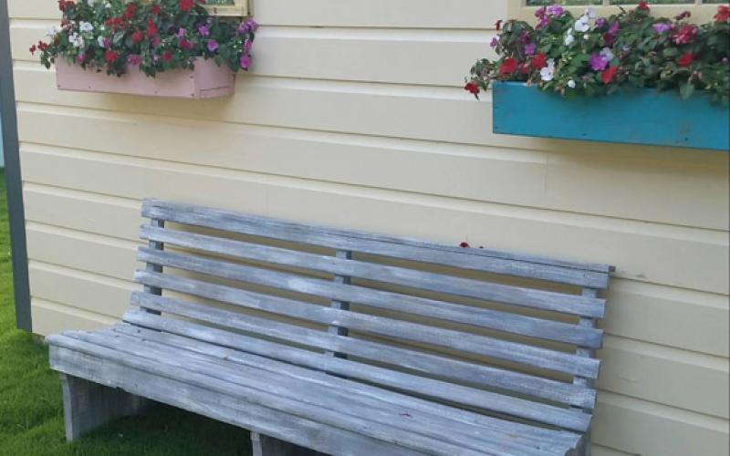 A wooden bench sits in front of a wall with colorful flower boxes.