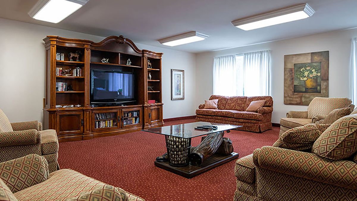 A cozy living room with a large wooden entertainment center, sofas, and a glass coffee table on red carpeting.