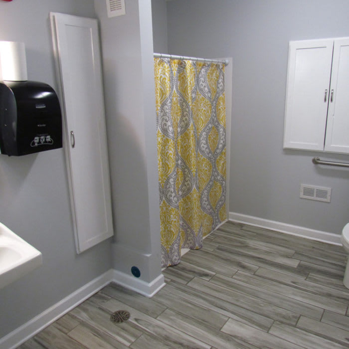 A modern public bathroom with a shower, sink, and wooden flooring.