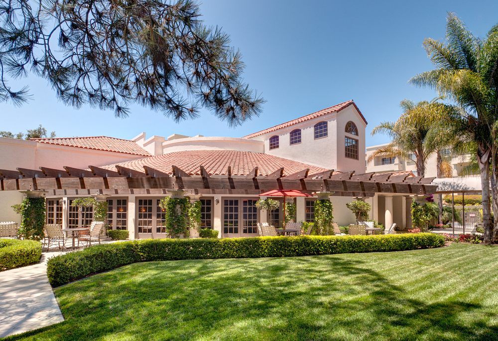 A beautiful house with Mediterranean architecture surrounded by lush greenery and a well-maintained lawn on a sunny day.
