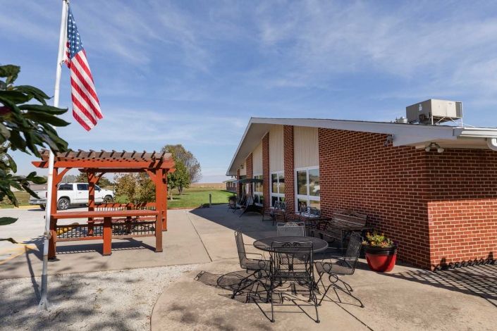 A sunny outdoor patio with seating, a pergola, and an American flag near a brick building.