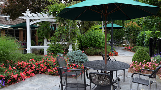 A serene outdoor patio setting with a table, chairs, and vibrant flowers surrounded by lush greenery.