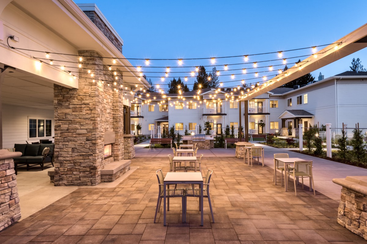 An inviting outdoor patio with string lights and modern furniture, set against a backdrop of architecture in the evening.