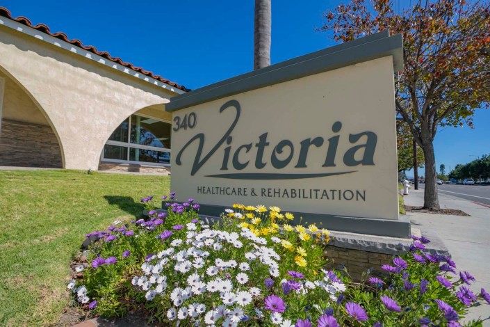 A sign for Victoria Health Care & Rehabilitation in front of a building with colorful flowers.