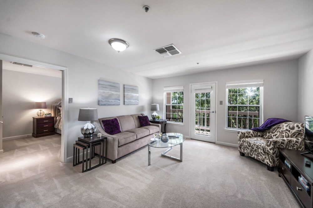 A modern living room with a sofa, coffee table, and large windows providing natural light.