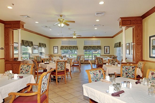 A well-lit restaurant dining area with neatly arranged tables and chairs, featuring ceiling fans and large windows.