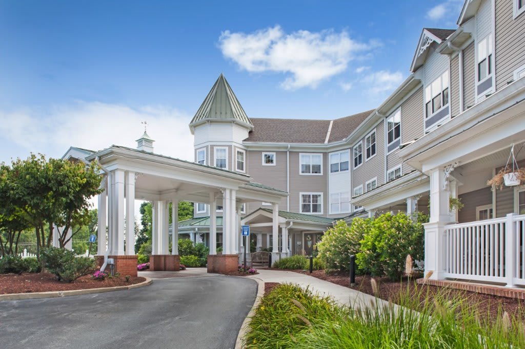 An exterior view of a retirement home with landscaped surroundings and a covered driveway.