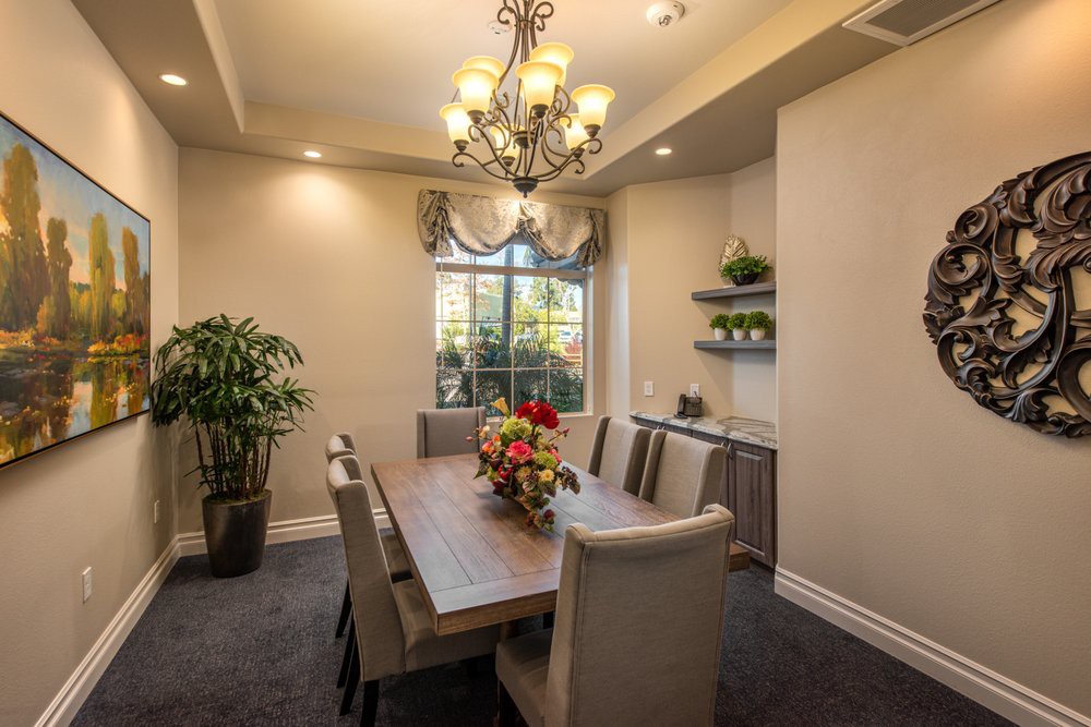 A cozy and elegant dining room featuring a large wooden table, comfortable upholstered chairs, a decorative chandelier, and lush green plants.