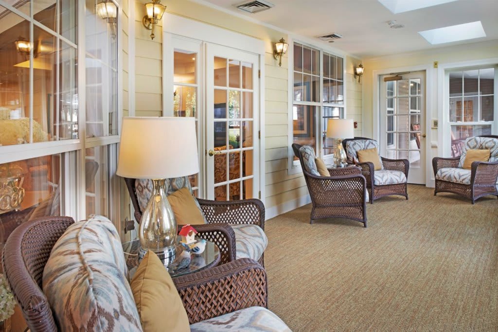 A cozy living room with wicker chairs, lamps, and large windows.