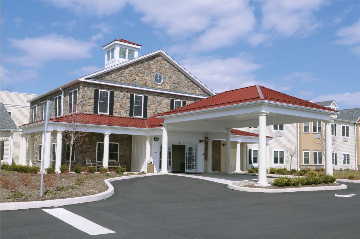 A building with a stone facade and red roof, featuring a covered entrance supported by columns.