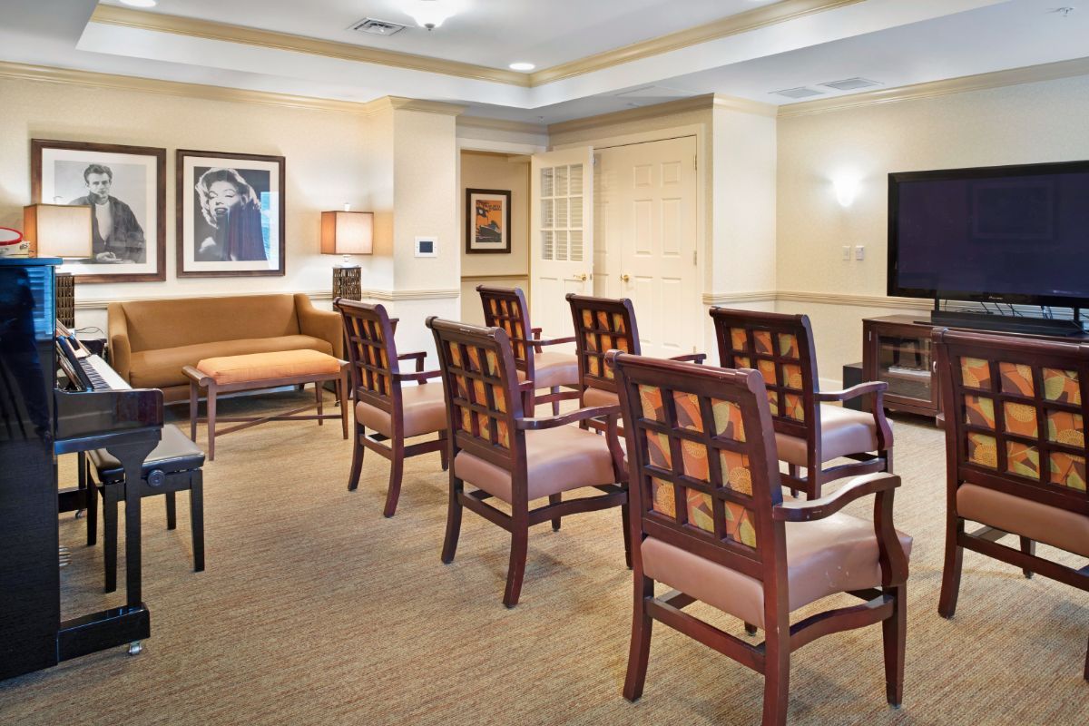 A waiting room with rows of chairs facing a television, decorated with framed artwork.
