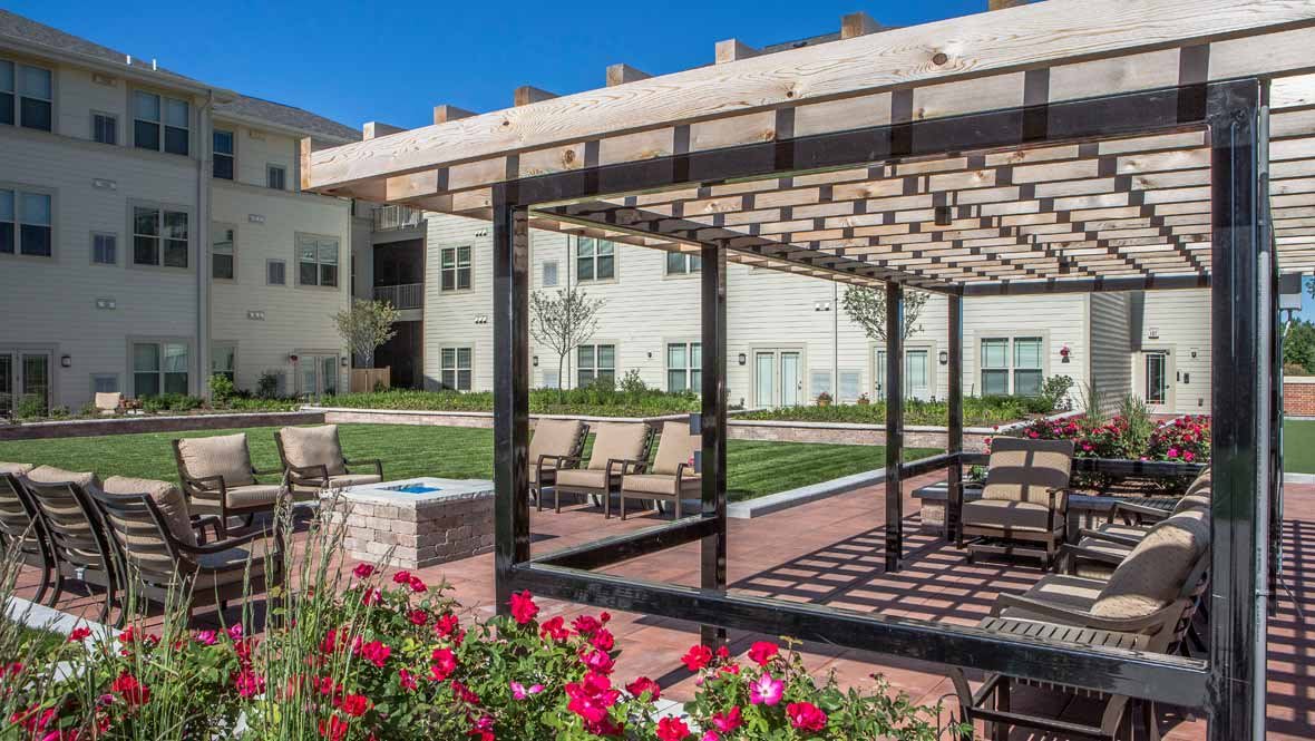 A pergola with outdoor seating surrounded by a garden in an apartment complex.