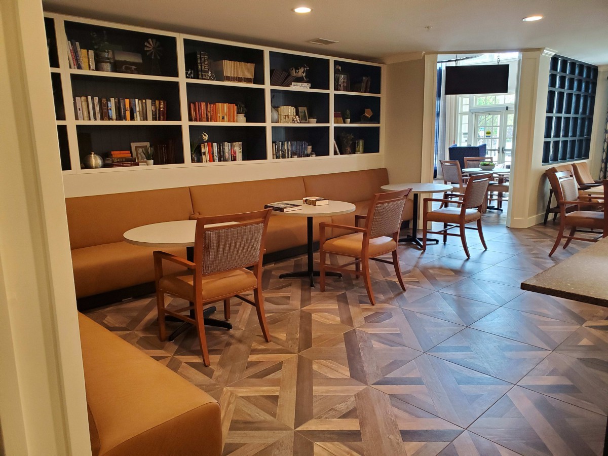 A cozy and modern cafe seating area with tables, chairs, and a bookshelf lining the wall.