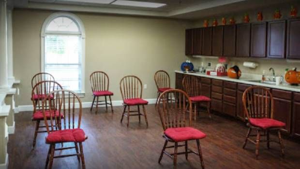 A small meeting room with red-cushioned chairs arranged in a circle, adjacent to a kitchenette area.