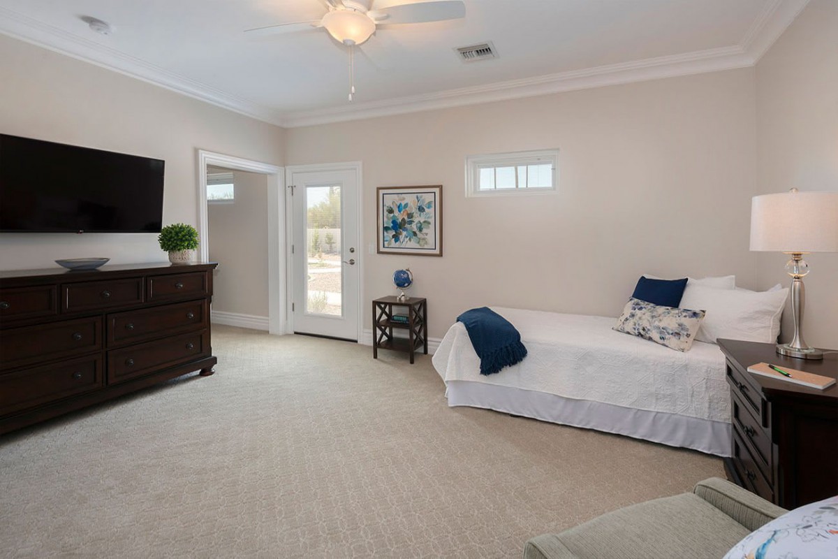 A spacious, modern bedroom featuring a single bed, dresser, and wall-mounted television.