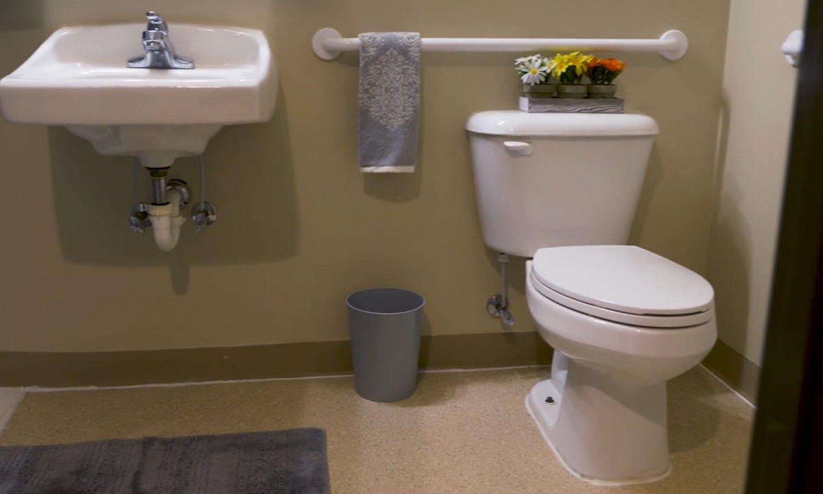 A clean and organized bathroom with a sink, toilet, towel, and decorative flowers.