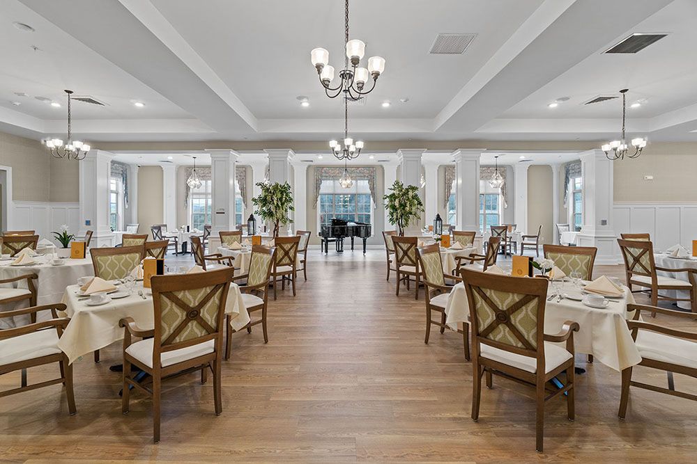 An elegant dining room setup with neatly arranged tables and chairs, adorned with chandeliers and natural lighting.