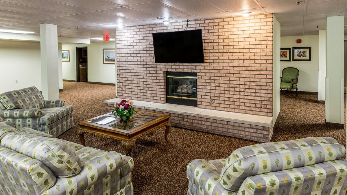 A cozy lobby area featuring a brick wall with a fireplace and mounted television, surrounded by comfortable seating and a coffee table.