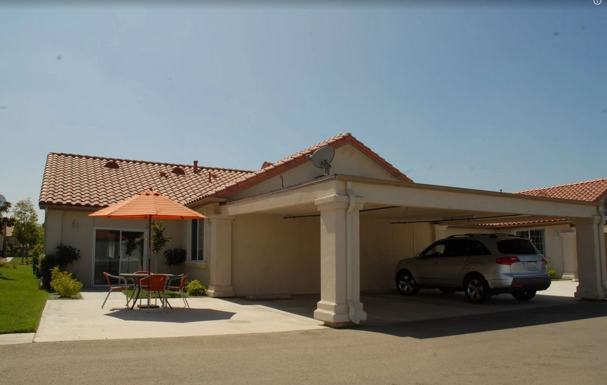 A suburban house with a car parked under a carport and a patio area with an orange umbrella.