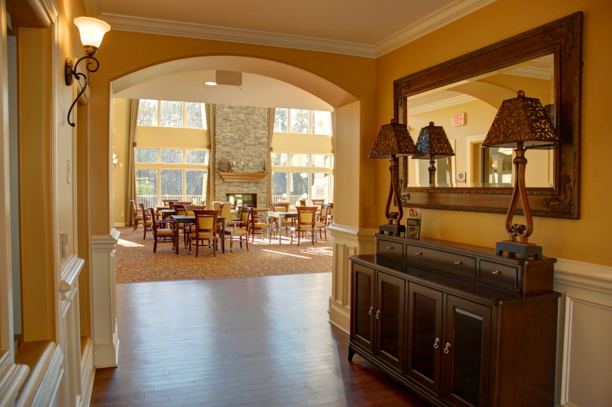 A cozy living space featuring a dining area with wooden furniture, large mirror, and a stone fireplace visible through an arched doorway.