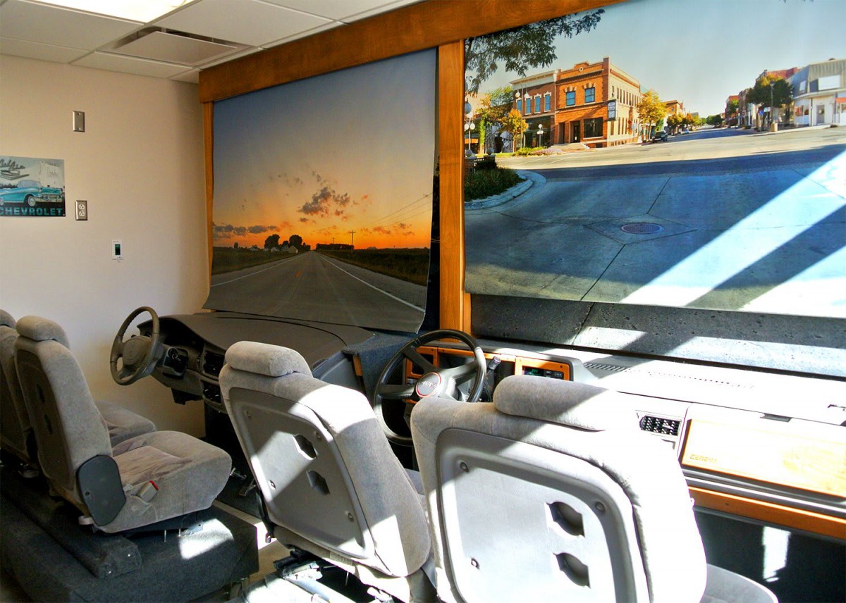 A driving simulator setup with steering wheels and car seats in a simulation room.