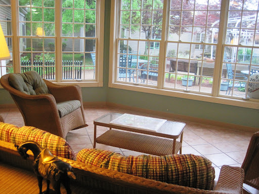A cozy living room with large windows, allowing natural light and a view of the greenery outside.