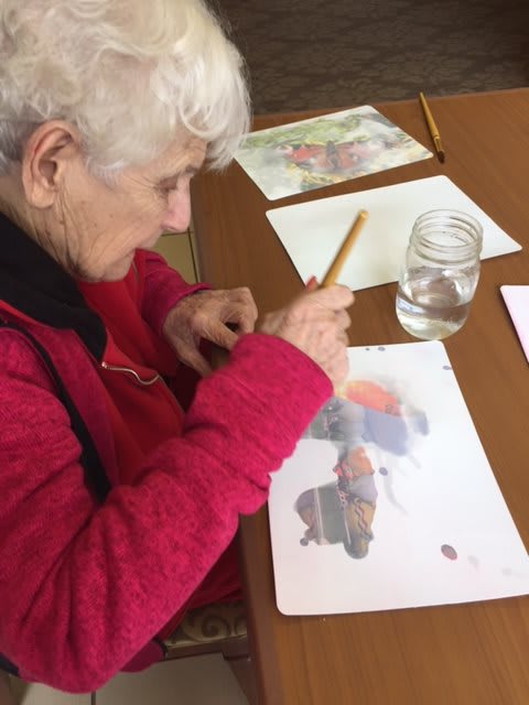 An elderly person engaged in watercolor painting at a table.