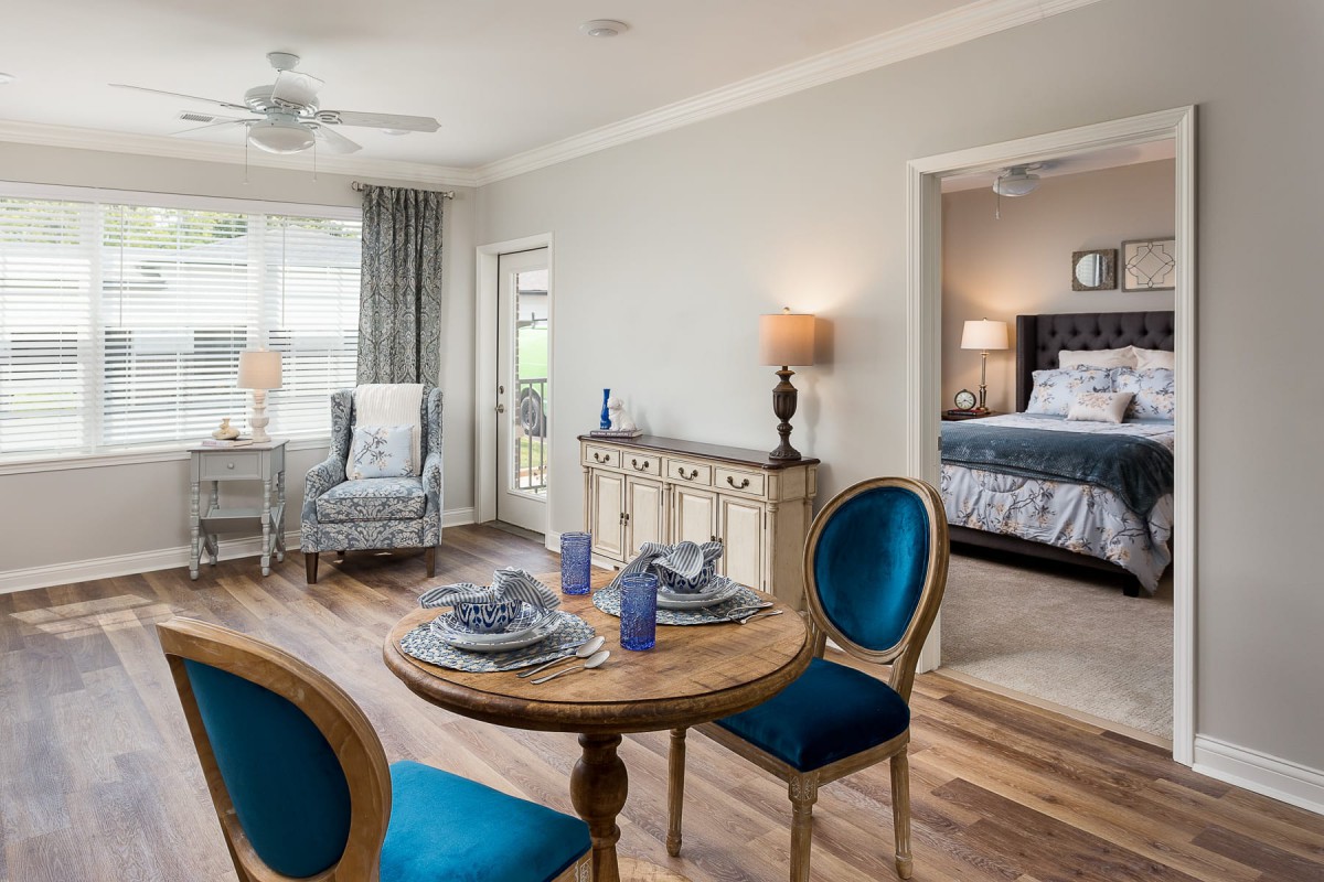 A cozy living space featuring a dining table with blue chairs, elegant decor, and an adjoining bedroom.
