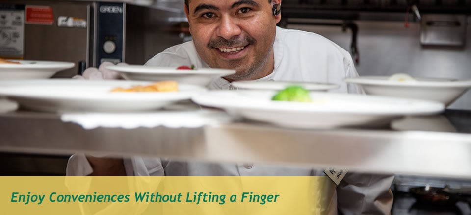 A smiling chef looks through a serving counter in a restaurant kitchen.