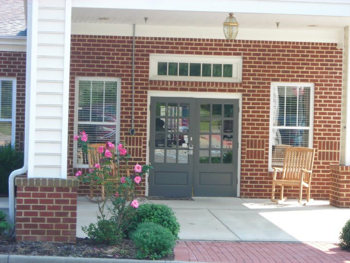 The image shows the entrance to a brick building with glass doors, windows, and flowers.